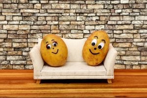two potatoes with faces sitting on a beige couch with a brick background