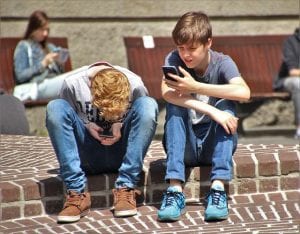 two young boys playing on their phones on a curbside.