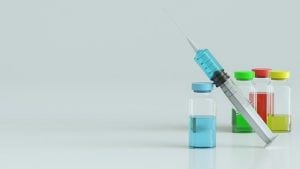 syringe with a blue substance in it with other bottles of red and yellow behind it.