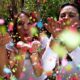 A group of people throwing and blowing confetti in the air outside.